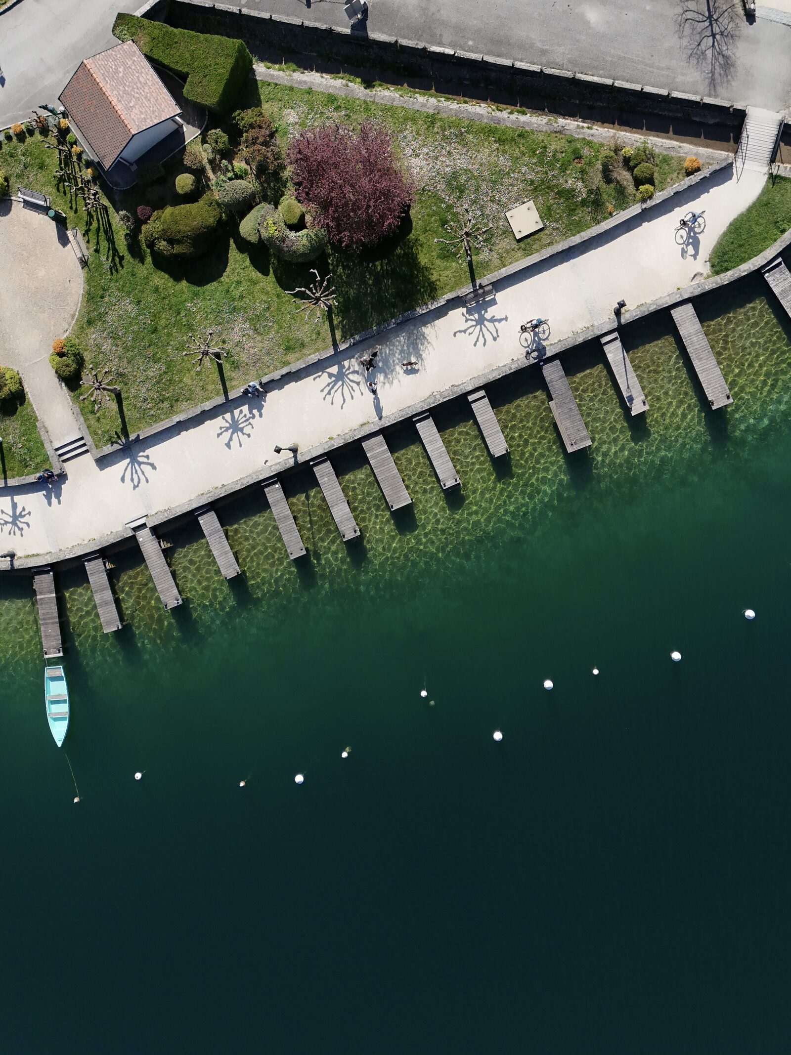 Top-down aerial of wooden jetties and clear green water along the Talloires promenade, Lake Annecy