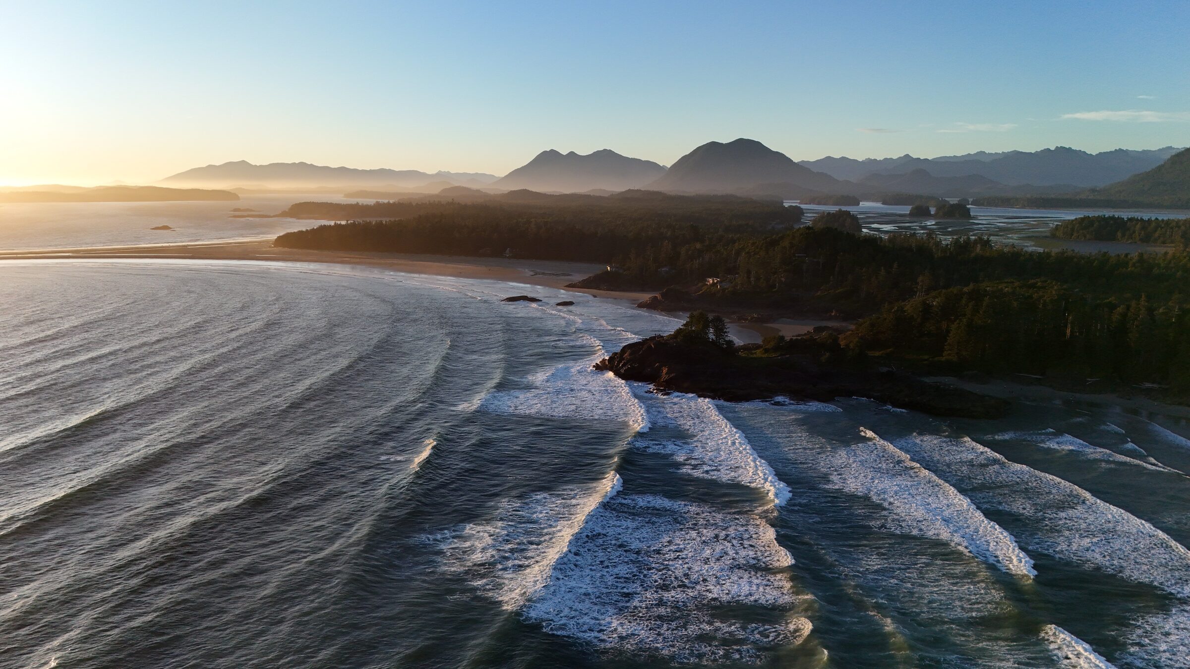 Golden-hour aerial of Pacific surf rolling onto the Tofino coastline