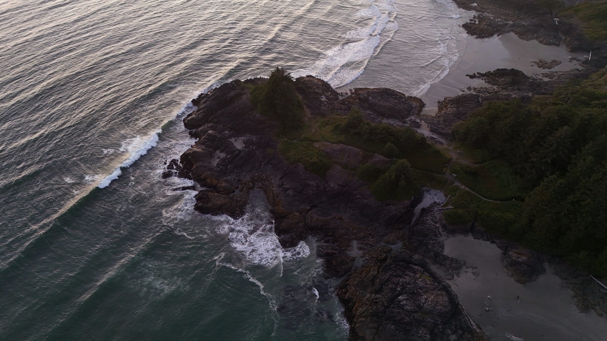 Aerial of a rocky forested headland at nightfall with surf breaking on both sides